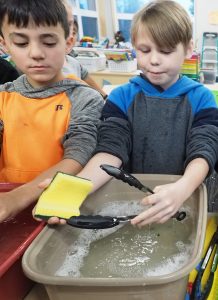 Two kids washing dishes in a classroom
