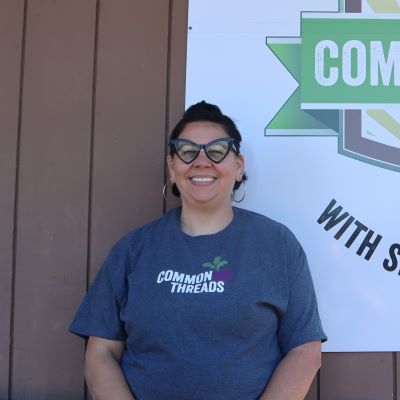 Becky Gutierrez stands in front of the Common Threads logo.
