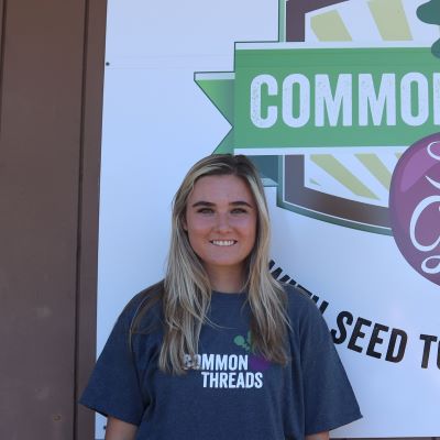 Mary Wilcox stands in front of the Common Threads logo.